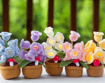 May include: A collection of six crochet flower arrangements in small brown baskets. The flowers are in various colors, including blue, purple, white, pink, and yellow. Each arrangement has green leaves and a small red and white mushroom.
