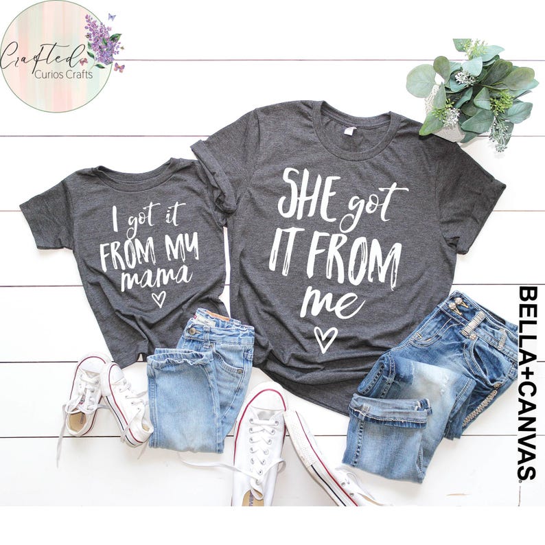 Puede incluir: Dos camisetas grises con texto blanco. La camiseta m&aacute;s grande dice "SHE got IT FROM me" con un coraz&oacute;n. La camiseta m&aacute;s peque&ntilde;a dice "I got it FROM MY mama" con un coraz&oacute;n.