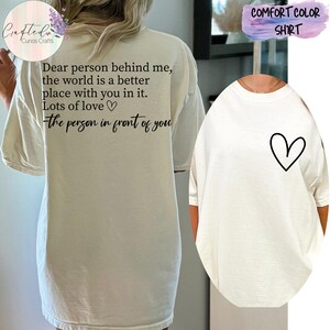 May include: White oversized t-shirt with a black graphic on the back that reads "Dear person behind me, the world is a better place with you in it. Lots of love - the person in front of you". The front of the shirt has a small black heart graphic.