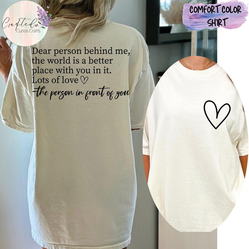 May include: White oversized t-shirt with a black graphic on the back that reads "Dear person behind me, the world is a better place with you in it. Lots of love - the person in front of you". The front of the shirt has a small black heart graphic.