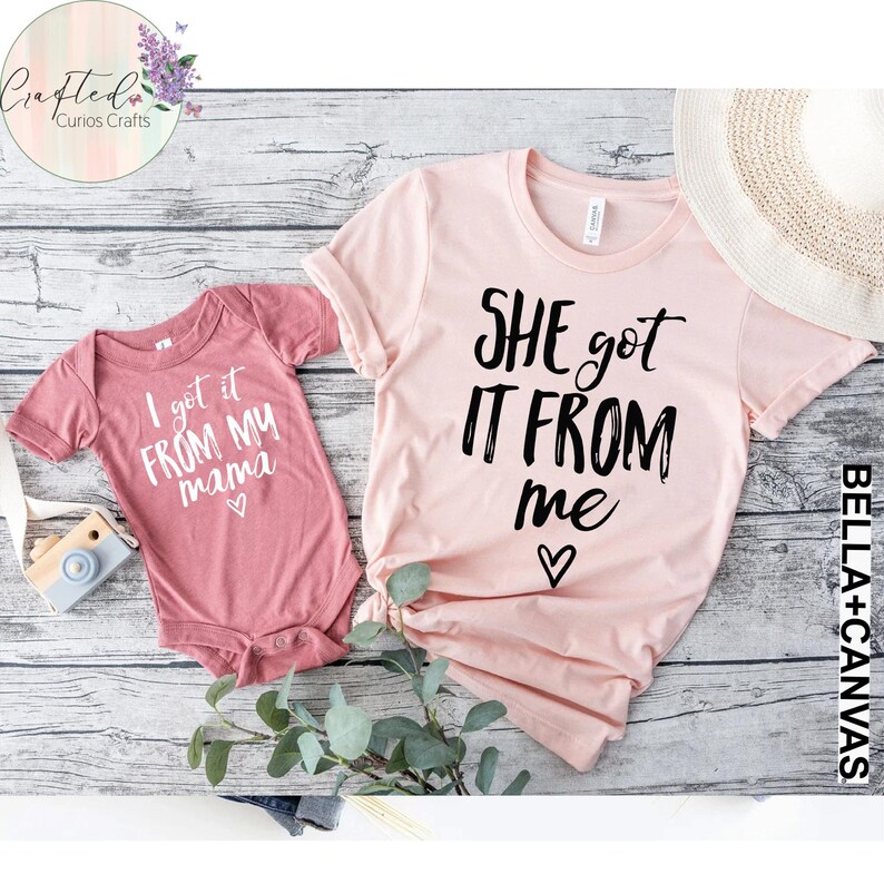 Puede incluir: Dos camisetas rosas y rojas con un dise&ntilde;o a juego. La camiseta m&aacute;s grande dice "SHE got IT FROM me" con un coraz&oacute;n. La camiseta m&aacute;s peque&ntilde;a dice "I got it FROM MY mama" con un coraz&oacute;n.