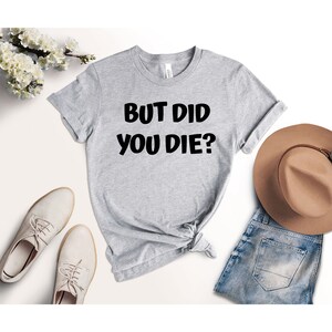May include: Gray t-shirt with black text that reads "But Did You Die?"