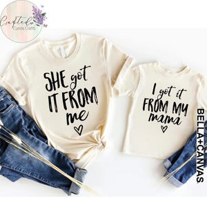 Puede incluir: Dos camisetas de color crema con texto negro. La camiseta m&aacute;s grande dice "SHE got IT FROM me" con un coraz&oacute;n. La camiseta m&aacute;s peque&ntilde;a dice "I got it FROM MY mama" con un coraz&oacute;n.
