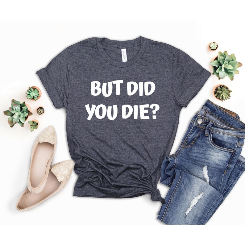 May include: A dark heather grey t-shirt with the text "BUT DID YOU DIE?" printed in white.