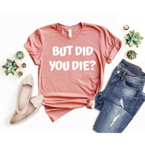 May include: A pink t-shirt with the text "But Did You Die?" in white lettering.