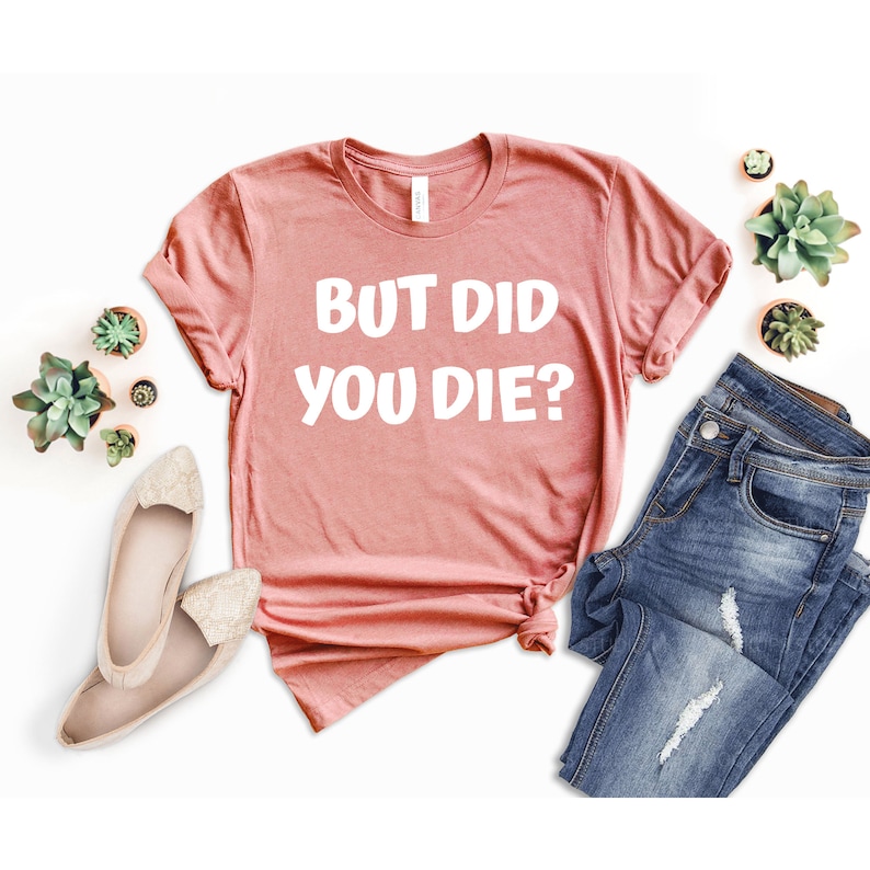 May include: A pink t-shirt with the text "But Did You Die?" in white lettering.
