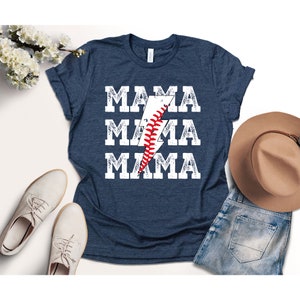 以下が含まれることがあります： 紺色のTシャツに、くたびれた白のグラフィックで「MAMA」という文字が3回繰り返されています。グラフィックの中央には、野球の縫い目が施された稲妻があります。