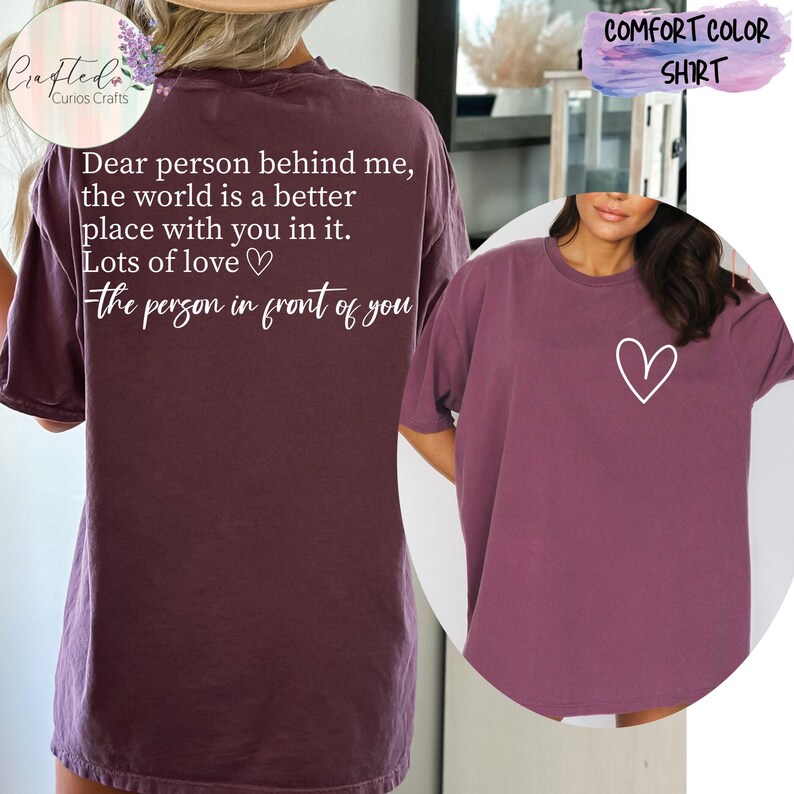 May include: A mauve colored t-shirt with a white heart on the front and a message on the back that reads "Dear person behind me, the world is a better place with you in it. Lots of love the person in front of you".