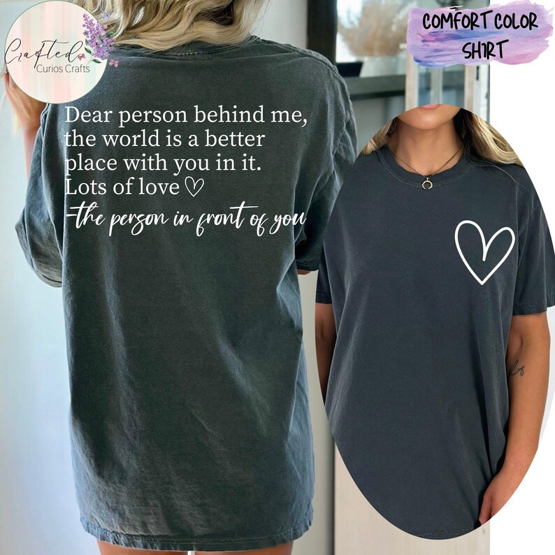 May include: A dark gray t-shirt with the text "Dear person behind me, the world is a better place with you in it. Lots of love - the person in front of you" on the back and a white heart on the front.