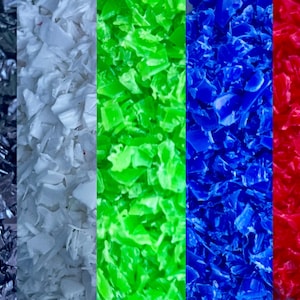 Può includere: Una composizione verticale di cinque colonne di pezzi di plastica colorati di forma irregolare. I colori includono nero, bianco, verde, blu e rosso. I pezzi sembrano essere materiali riciclati o riutilizzati.