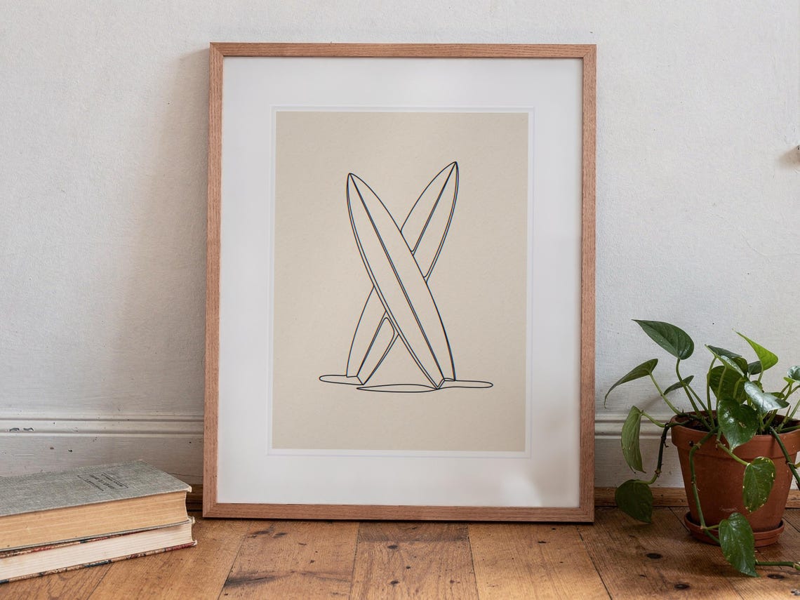 Crossed Surfboards Line print in a Red Oak frame with a white mat, standing on the floor, leaning back slightly against the wall in a living room floor lean.