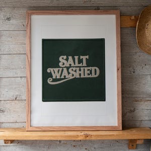 Salt Washed Patch print in a Red Oak frame with a white mat, leaning on the shelf against the wall in a surf shack bedroom.