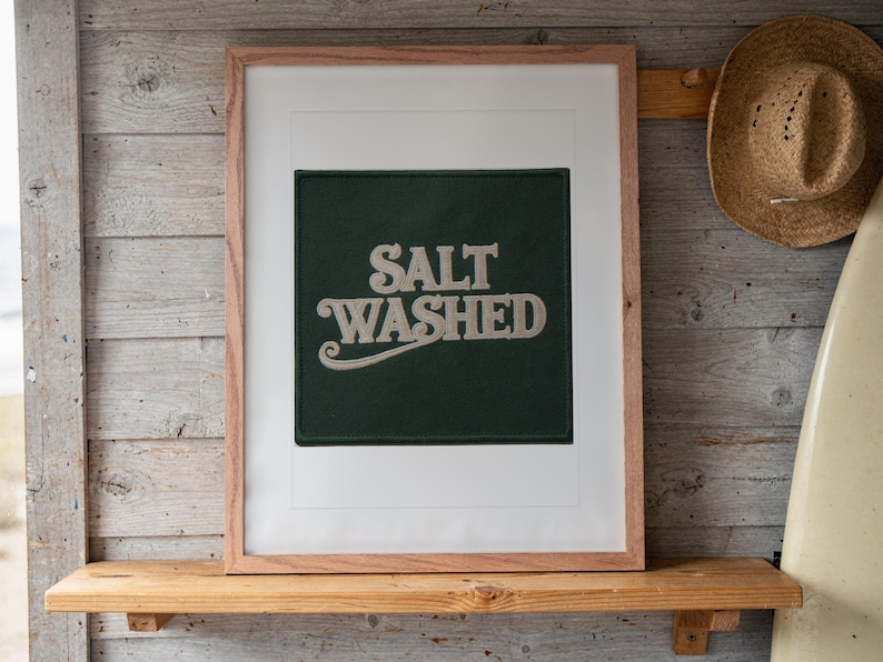 Salt Washed Patch print in a Red Oak frame with a white mat, leaning on the shelf against the wall in a surf shack bedroom.