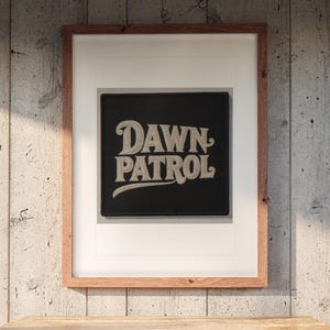 Dawn Patrol Patch print in a Red Oak frame with a white mat, hanging above the dresser in a surf shack bedroom.