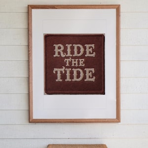 Ride the Tide Patch print in a Red Oak frame with a white mat, hanging above the table in a screened beach porch.