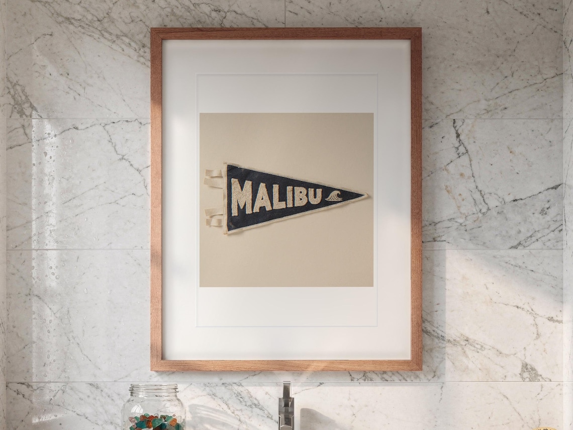 Malibu Surf Pennant print in a Red Oak frame with a white mat, hanging above the vanity in a bright bathroom.
