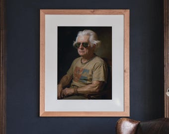 May include: A framed portrait of an older individual with white hair wearing dark sunglasses and a tan t-shirt with a graphic print. The artwork is encased in a light-toned wooden frame with a white mat, displayed against a dark wall.