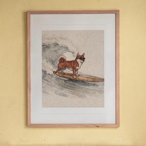 Shiba Inu Surfing print in a Red Oak frame with a white mat, hanging above the bookshelf in a kids' room.