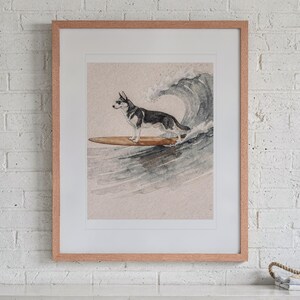 May include: A framed watercolor print featuring a black and white husky dog wearing sunglasses while standing on a brown surfboard riding a large ocean wave. The artwork is enclosed in a light-colored wooden frame with a white mat border.