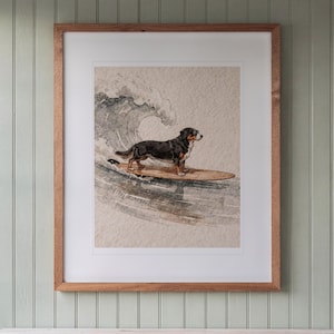 Bernese Mountain Dog Surfing print in a Red Oak frame with a white mat, hanging above the console in a beach cottage entryway.