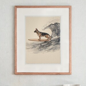 May include: A framed watercolor print featuring a German Shepherd standing on a wooden surfboard in front of a large, crashing ocean wave. The artwork is encased in a light-toned wooden frame with a white mat, displaying a neutral background.