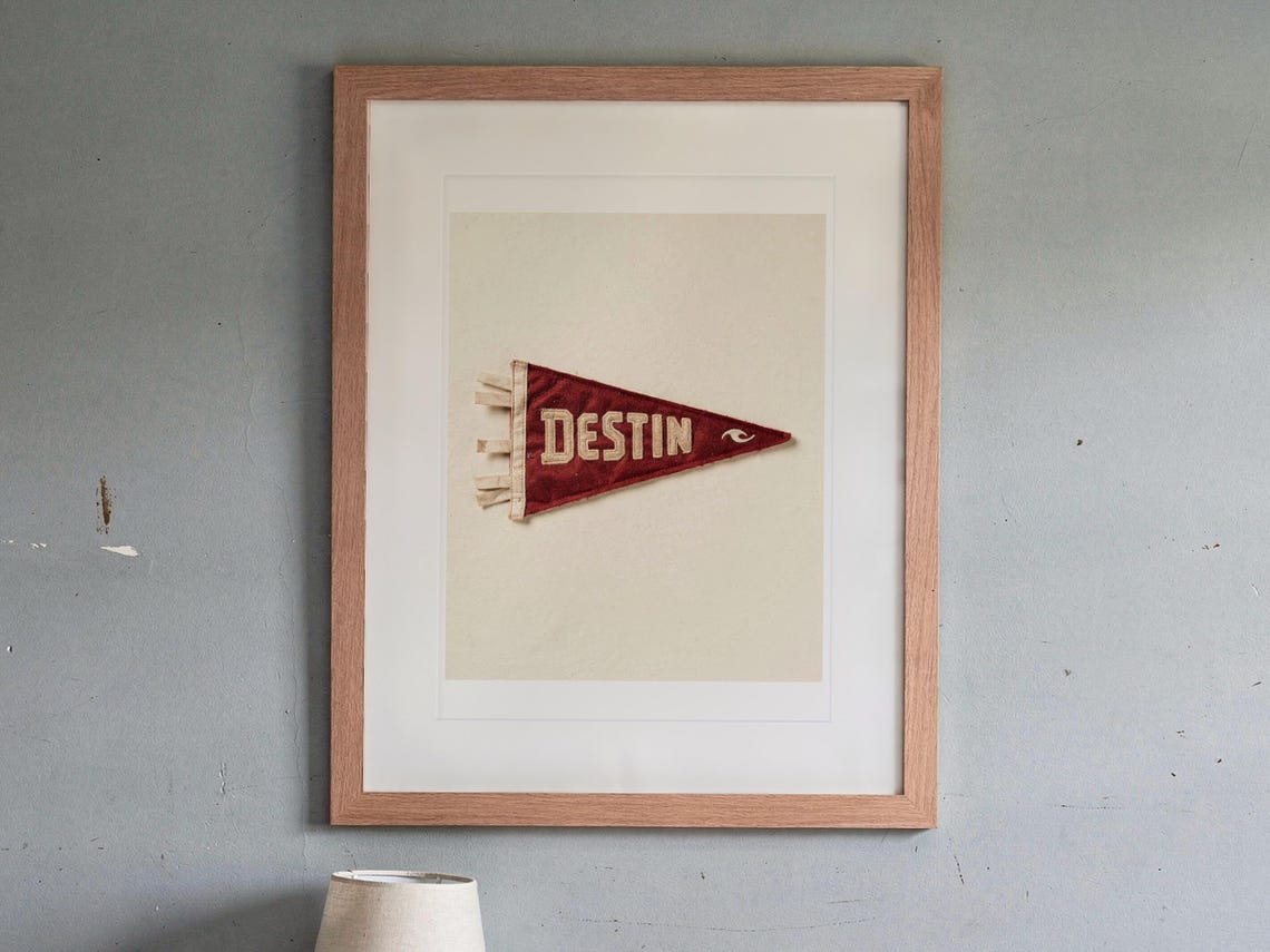 Destin print in a Red Oak frame with a white mat, hanging above the bedside table in a calm bedroom.