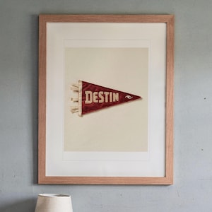 Destin print in a Red Oak frame with a white mat, hanging above the bedside table in a calm bedroom.