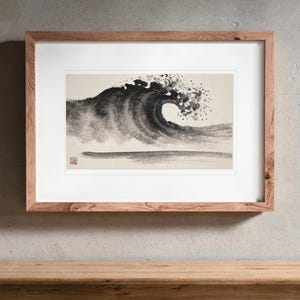 May include: A framed ink wash painting on paper depicting a large, curling ocean wave in shades of black and gray. The artwork features a single red square seal in the bottom left corner and is enclosed in a light brown wooden frame.