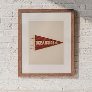 Oceanside Surf Pennant print in a Red Oak frame with a white mat, hanging above the cubbies in a mudroom.