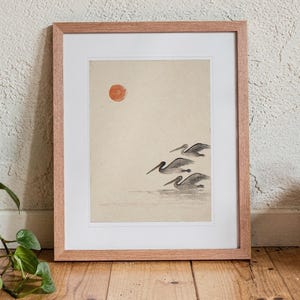 Pelicans Ink Style print in a Red Oak frame with a white mat, standing on the floor, leaning back slightly against the wall in a living room floor lean.