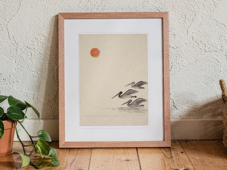 Pelicans Ink Style print in a Red Oak frame with a white mat, standing on the floor, leaning back slightly against the wall in a living room floor lean.