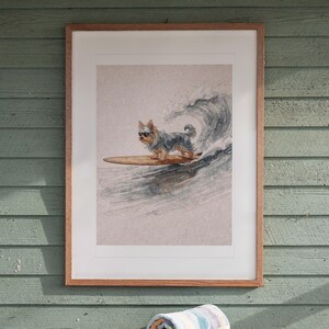 Yorkshire Terrier Surfing printable art, shown printed in a Red Oak frame with a white mat, hanging above the table in a screened beach porch.