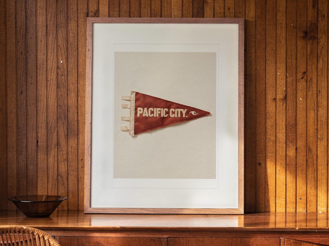 Pacific City Surf Pennant print in a Red Oak frame with a white mat, hanging above the sideboard in a mid-century living room.