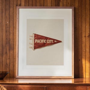 Pacific City Surf Pennant print in a Red Oak frame with a white mat, hanging above the sideboard in a mid-century living room.