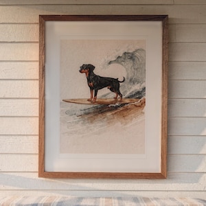 Doberman Surfing print in a Red Oak frame with a white mat, hanging above the bench in a screened beach porch.