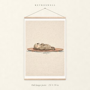 Sea Otter on Surfboard oak hanger poster, 24 by 36 inches, with natural wood rails and a hanging cord.