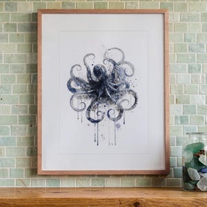 May include: A framed art print featuring a dark blue watercolor illustration of an octopus with ink-like splatters and drips, centered on a white background within a light wood frame, displaying a detailed marine creature design.