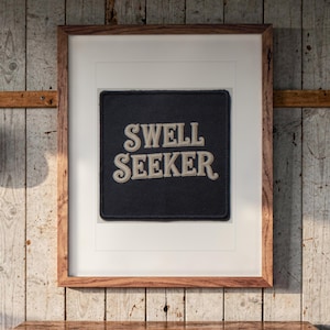 Swell Seeker Patch print in a Red Oak frame with a white mat, hanging above the dresser in a surf shack bedroom.