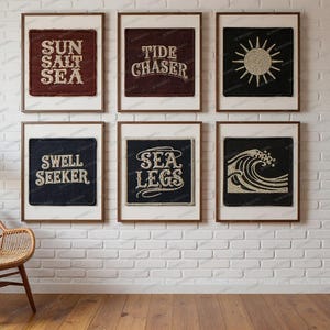 Pode incluir: Seis impressões de arte emolduradas com texto e imagens de tema náutico penduradas em uma parede de tijolos brancos. As impressões apresentam frases como "Sun Salt Sea" e "Sea Legs", juntamente com um desenho de sol e onda. Uma cadeira de vime e uma planta estão em primeiro plano.