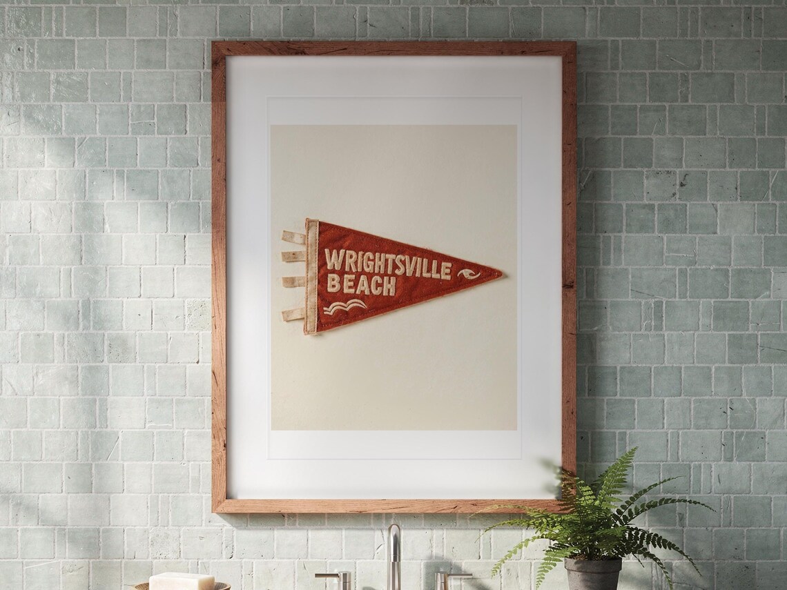 Wrightsville Beach Surf Pennant print in a Red Oak frame with a white mat, hanging above the vanity in a bright bathroom.