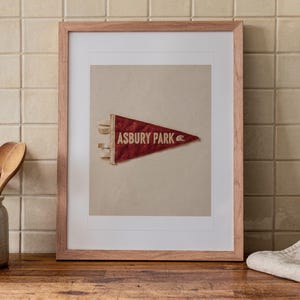 Asbury Park Surf Pennant print in a Red Oak frame with a white mat, leaning on the counter against the backsplash in a cottage kitchen.