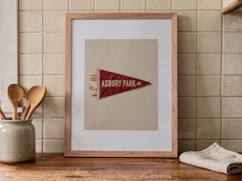 Asbury Park Surf Pennant print in a Red Oak frame with a white mat, leaning on the counter against the backsplash in a cottage kitchen.