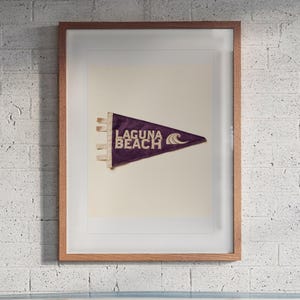 Laguna Beach print in a Red Oak frame with a white mat, hanging above the workbench in a surf garage.