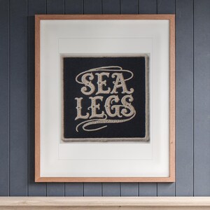 Sea Legs Patch printable art, shown printed in a Red Oak frame with a white mat, hanging above the bench in a mudroom.