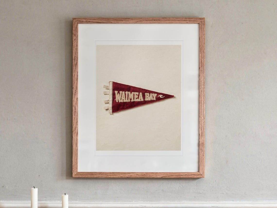 Waimea Bay Surf Pennant print in a Red Oak frame with a white mat, hanging above the sideboard in a dining room.