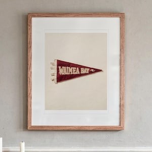 Waimea Bay Surf Pennant print in a Red Oak frame with a white mat, hanging above the sideboard in a dining room.
