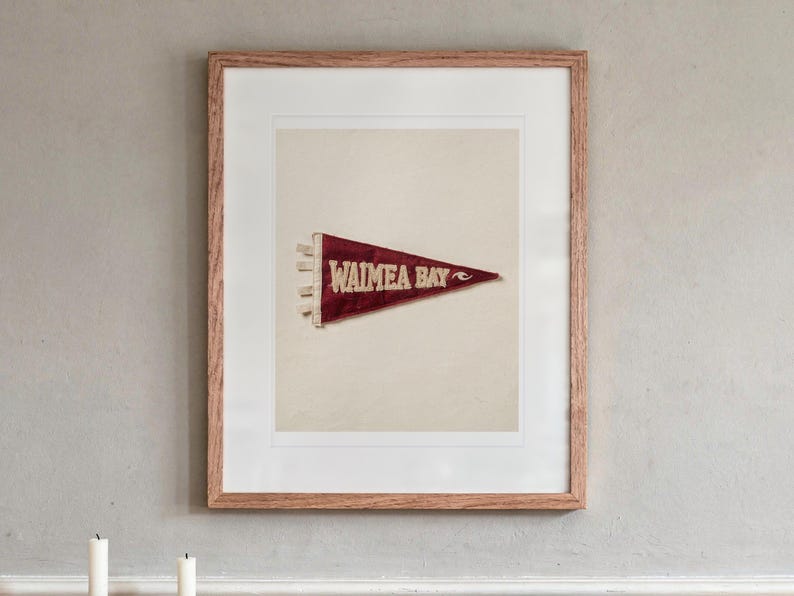 Waimea Bay Surf Pennant print in a Red Oak frame with a white mat, hanging above the sideboard in a dining room.