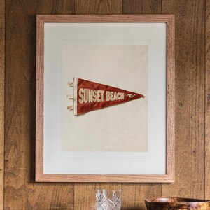 Sunset Beach print in a Red Oak frame with a white mat, hanging above the cabinet in a game room.