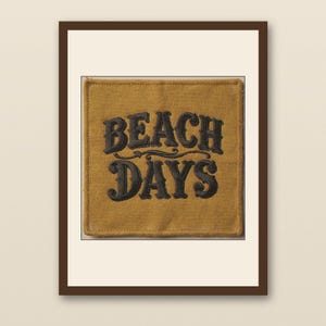 May include: A framed print featuring the words "BEACH DAYS" in a decorative, dark gray font on a mustard yellow background. The print is set within a white mat and a dark brown frame, creating a vintage aesthetic.