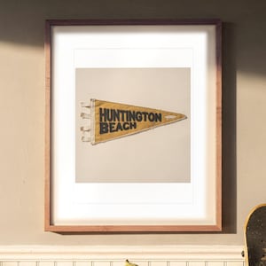 Huntington Beach Surf Pennant print in a Red Oak frame with a white mat, hanging above the sideboard in a dining room.